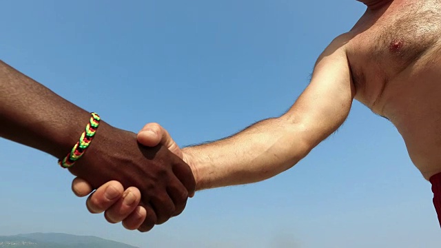 在蓝天上，两个无法辨认的黑人和白人男子握手。关闭视图。平等视频下载