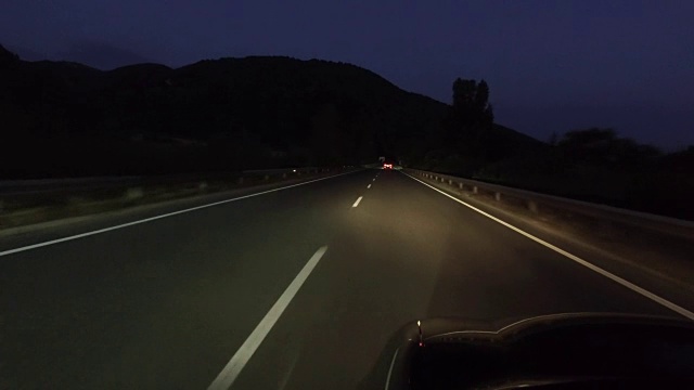 在漆黑的夜晚开着前灯行驶在乡村道路上视频素材