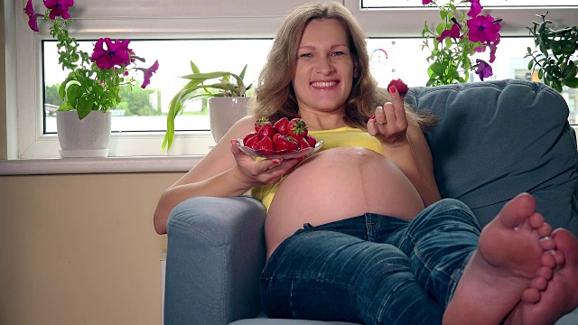怀孕的年轻雌性坐在沙发上吃着多汁的草莓视频素材