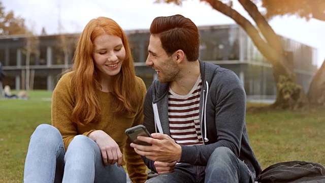 年轻的男人和女人坐在公园里看电话上的东西视频素材