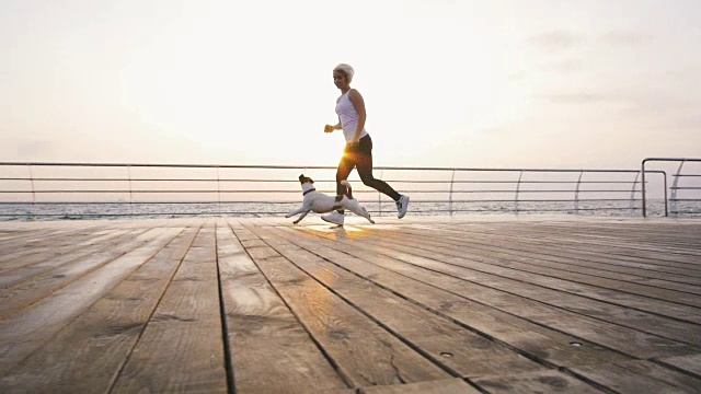 年轻女子和可爱的狗杰克罗素在海边跑步，慢镜头视频素材