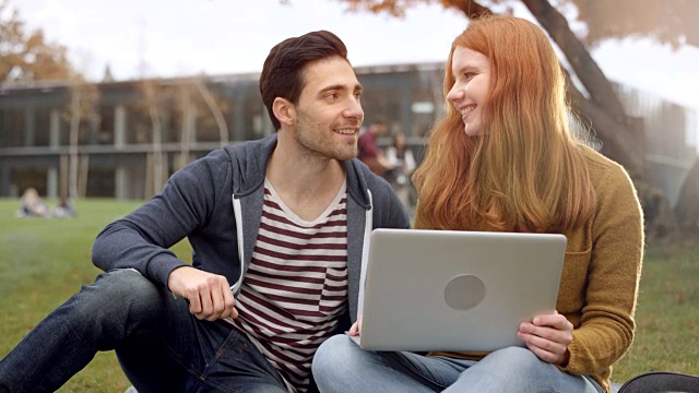 男女学生坐在草坪上，讨论着笔记本电脑上的东西视频素材