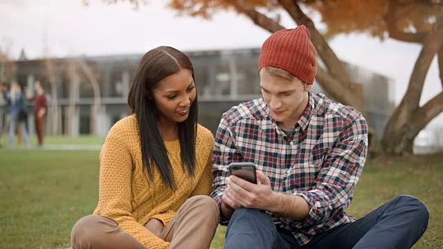 多种族女学生和她的白人男性朋友坐在公园里看手机视频素材