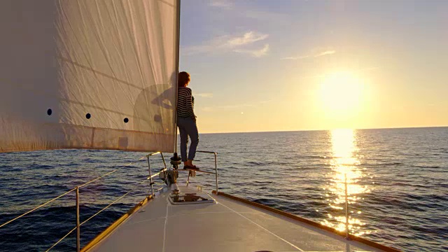 SLO MO女人在一艘帆船上指着夕阳视频素材