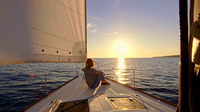 日落时分，一个女人坐在一艘帆船的船头上视频素材