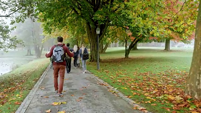 一个秋天的早晨，一个白人男学生骑着滑板经过一群穿过公园的学生视频下载