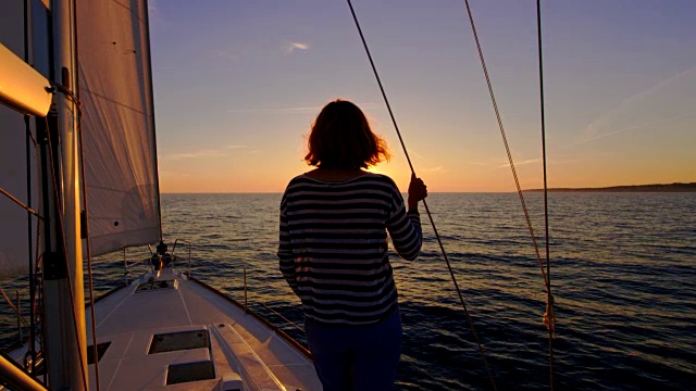 女人在一艘帆船的甲板上观察美丽的日落视频素材