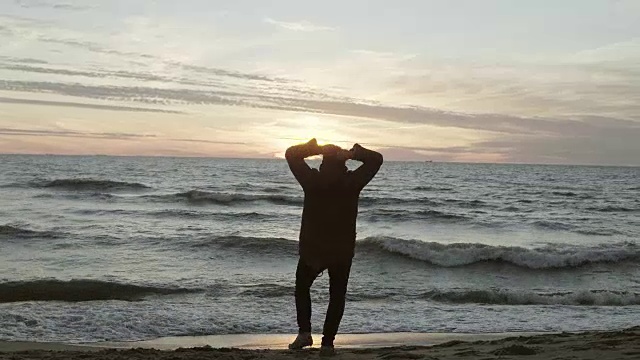 男人在黄昏的海滩上跑步，扔沙子。男在波涛汹涌的海边享受自然风光视频素材