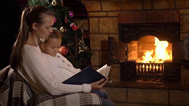 妈妈和小女儿在壁炉和圣诞树旁看书视频素材