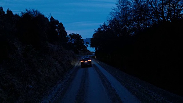 鸟瞰图汽车行驶在乡村道路上，SUV驾驶在黄昏与前灯穿过松树视频素材