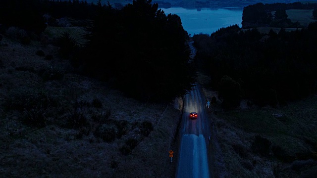 鸟瞰图汽车行驶在乡村道路上，SUV驾驶在黄昏与前灯穿过松树视频素材