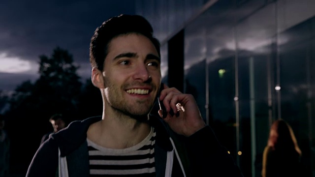一个年轻人晚上在大学大楼边打电话视频素材