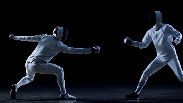 两名装备齐全的职业击剑手熟练地用剑剑格斗。拍摄在慢动作和孤立的黑色背景。视频素材