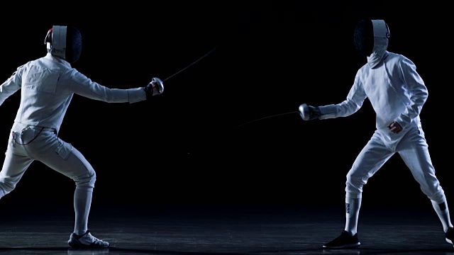 两位职业击剑选手在花剑比赛中展示了高超的剑术。一个击剑者重新获得快速弗莱切攻击。拍摄孤立的黑色背景与冷色调和慢动作。视频素材