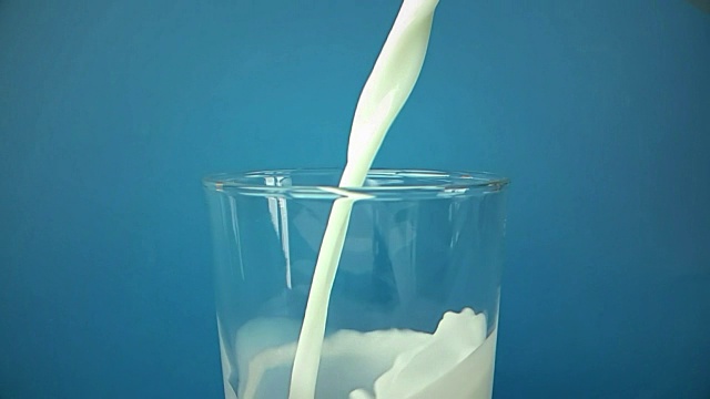 蓝色背景下，新鲜的白色牛奶倒入杯中，慢镜头拍摄，饮食和健康营养视频素材