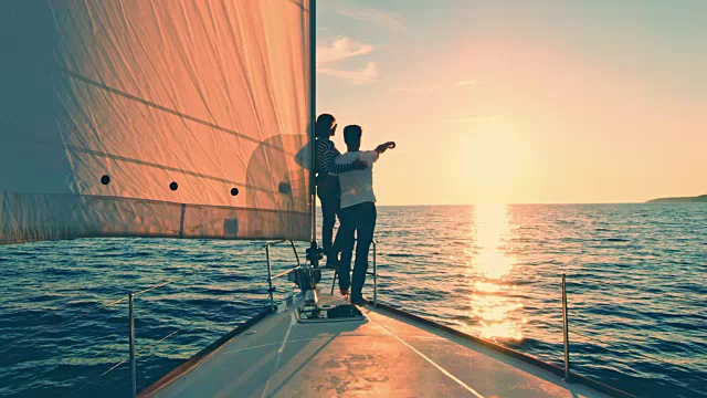 日落时分，一对夫妇在一艘帆船上指着地平线视频素材