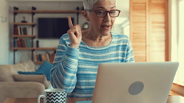一个成熟的女人一边在家上网一边在笔记本电脑上打字。视频素材