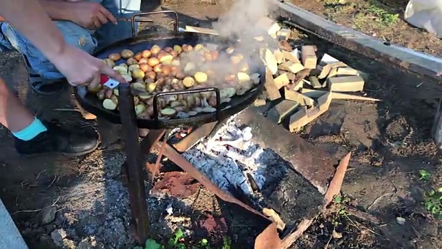 准备烤土豆和培根。土豆和猪油正在烤架上。火在燃烧，煤在冒烟。视频素材