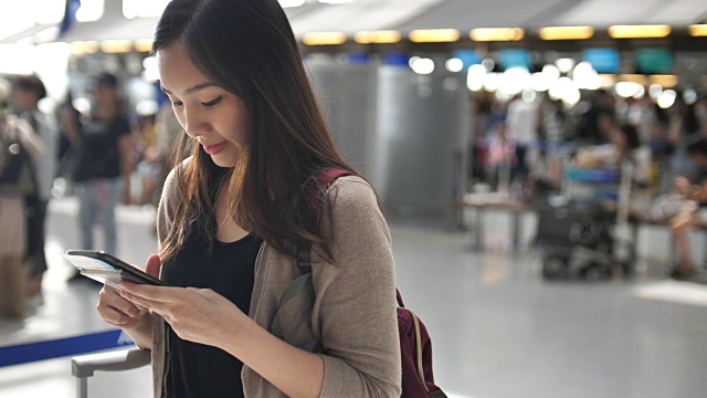 一名女子在机场办理登机手续时使用智能手机视频下载