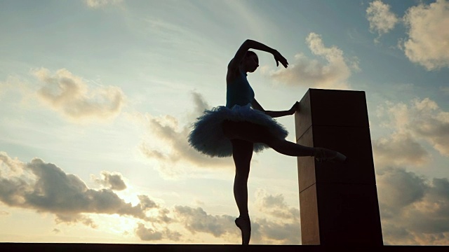 芭蕾舞女演员的剪影在芭蕾舞短裙和尖在戏剧性的天空背景。年轻漂亮的女人在做伸展运动。女孩站着不动。缓慢的运动。常平架枪视频素材