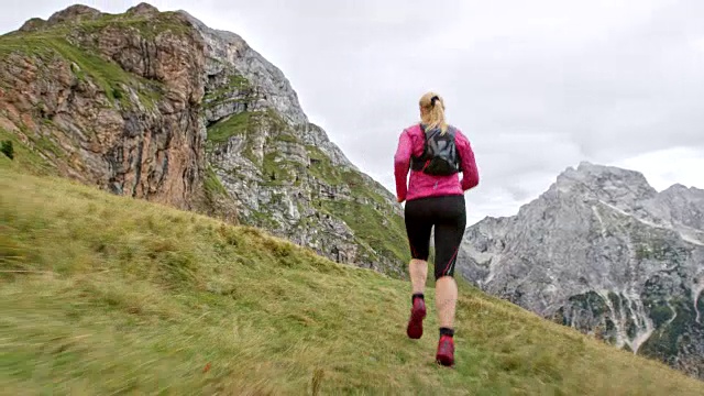 跟随着一个在高高的山脊上长满草的小道上跑步的女性视频素材
