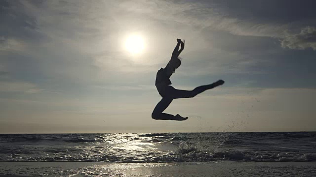 年轻女子在休闲风格-牛仔和黑色上衣在海滩上做芭蕾。迷人的芭蕾舞演员在秋天的沙滩上练习伸展。慢动作视频素材