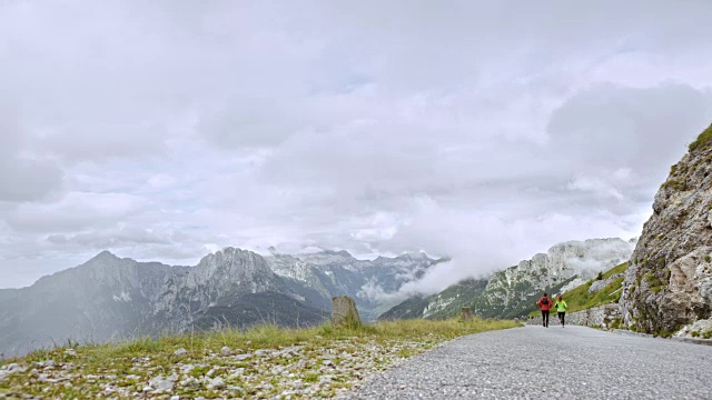 一男一女跑步者沿着柏油路下山，俯瞰附近的山峰视频素材