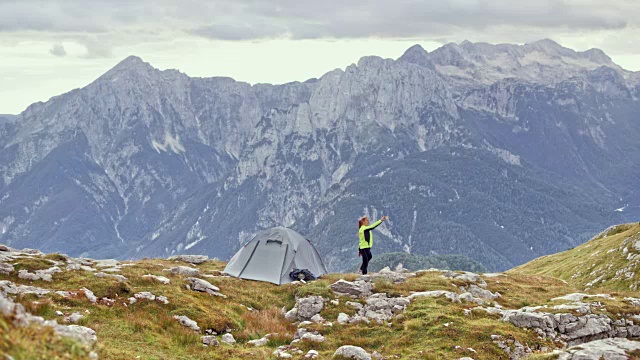 一个女人站在高山上她的帐篷旁边，拍下了令人惊叹的景色视频素材