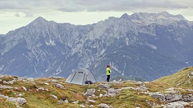 一个女人站在她的帐篷旁边拍照，在高高的山上有美丽的风景视频素材