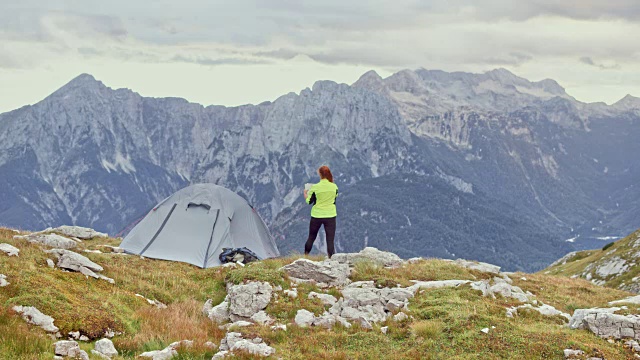 女徒步旅行者站在她的帐篷旁边，在高山上，检查她手中的地图视频素材