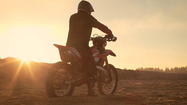 专业的FMX摩托车骑手旋转全油门手柄，开始在沙地越野赛道上骑行。风景优美的日落。视频素材
