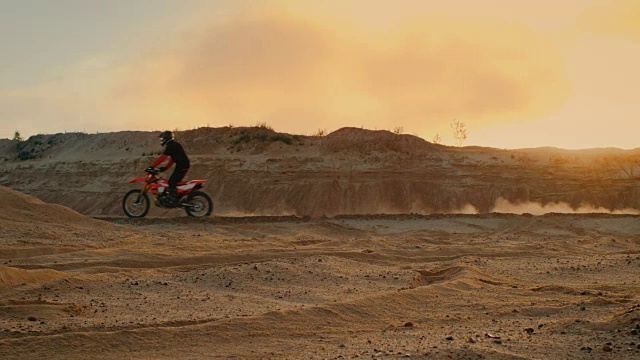 侧面拍摄的专业自行车骑手驾驶他的FMX摩托车在桑迪越野赛道上。风景优美的日落是背景。视频素材