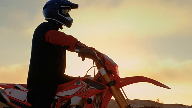 专业FMX摩托车骑手准备开始驾驶他的摩托车在坚硬的沙地越野地形。太阳设置。视频素材