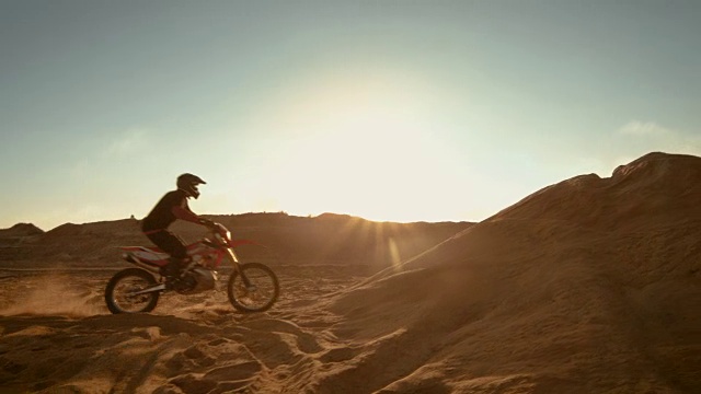 侧面镜头的专业摩托车越野赛摩托车骑手驾驶在沙丘和更远的越野轨道。这是《日落》，赛道上布满了烟雾。视频素材