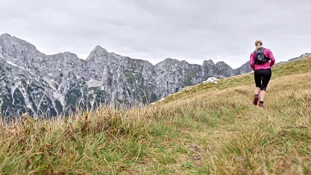 在高高的山脉中，一个女人跑过长满草的山脊视频素材