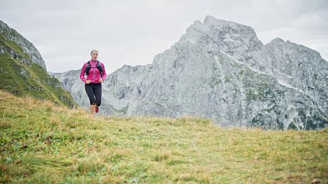 一名女性跑步者在一条长满草的小路上跑下山，沿途景色优美视频素材