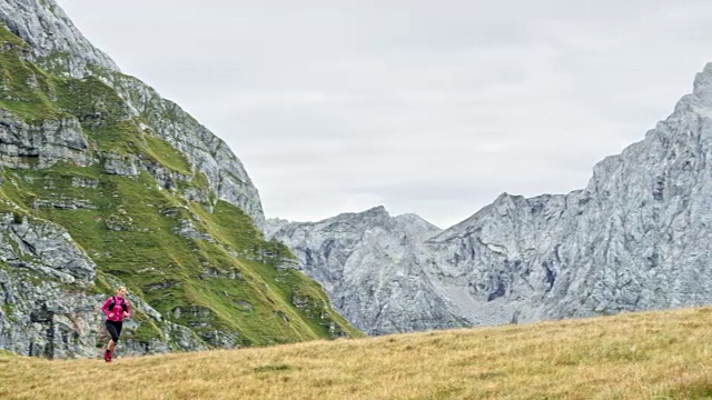 一名女性跑步者正在穿越长满草的山脊，俯瞰附近的山峰视频素材