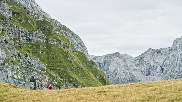 一个女人跑下长满草的山脊，俯瞰附近的山脉视频素材