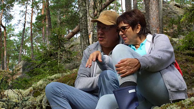 一对活跃的老年夫妇坐在一块岩石上，欣赏北方的森林视频素材
