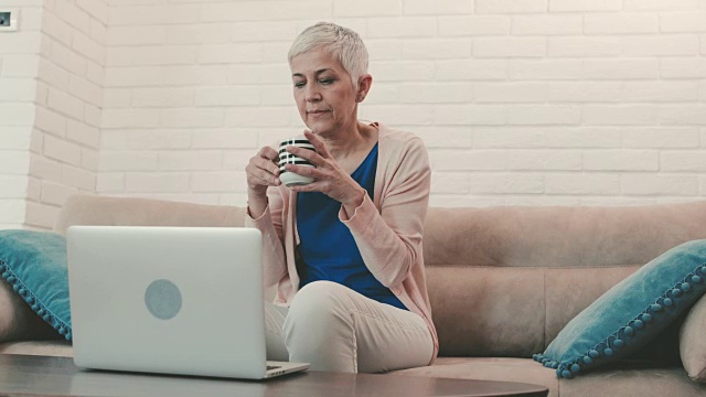 一个成熟的女人在家用笔记本电脑写完一封邮件后喝咖啡。视频素材