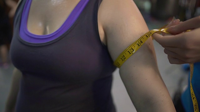 教练测量女性在健身房锻炼后的手臂，减肥计划的结果视频下载