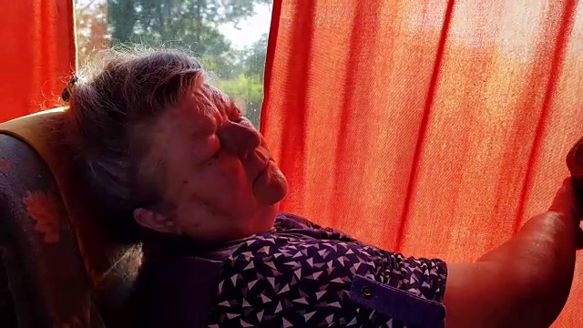 在长途旅行中，一位老妇人睡在车窗旁的公交车上。视频素材