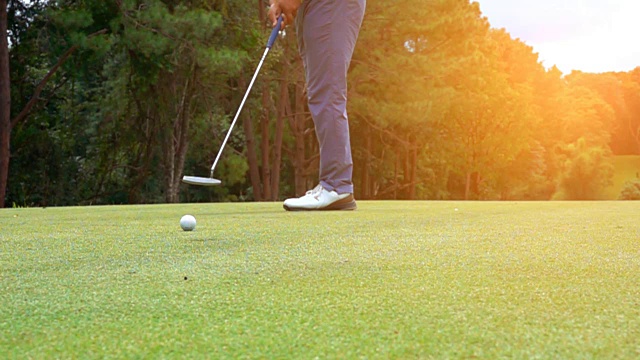 超级慢动作高尔夫球手把高尔夫球在果岭洞，以比赛的获胜者在日落视频素材