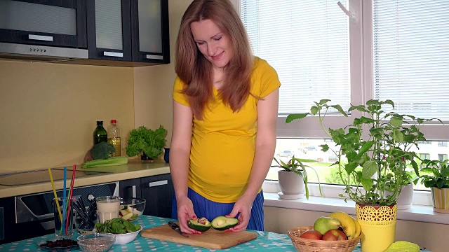 微笑孕妇切牛油果和看在厨房的相机视频素材