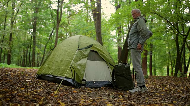 一个不错的老人站在森林里他的帐篷附近视频下载