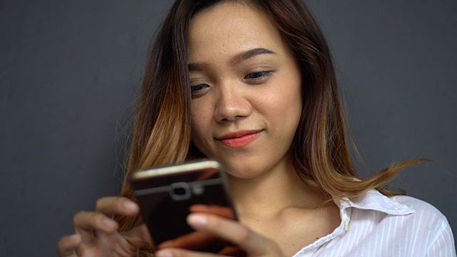 年轻的亚洲女子享受和微笑与她的智能手机视频素材