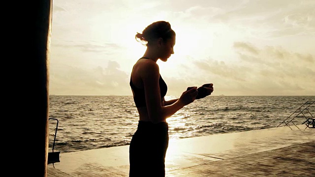 女运动员为拳击手套准备了她的拳头，她在太阳下站着，用绷带把拳头包起来。女拳击手在沙滩上用拳击包装纸包裹双手。眩光视频素材