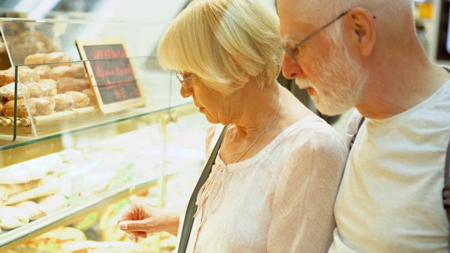 老年夫妇在购物中心购物。站在面包店的橱窗旁，挑选新鲜美味的糕点视频素材