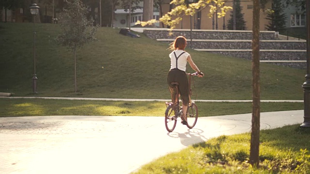 红发女子骑自行车在城市公园骑车后视镜视频素材