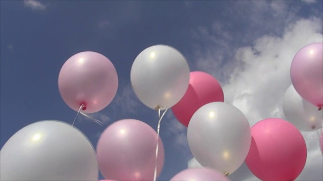 粉红色和白色的充气球在线上随风摆动着对着天空和云朵视频下载